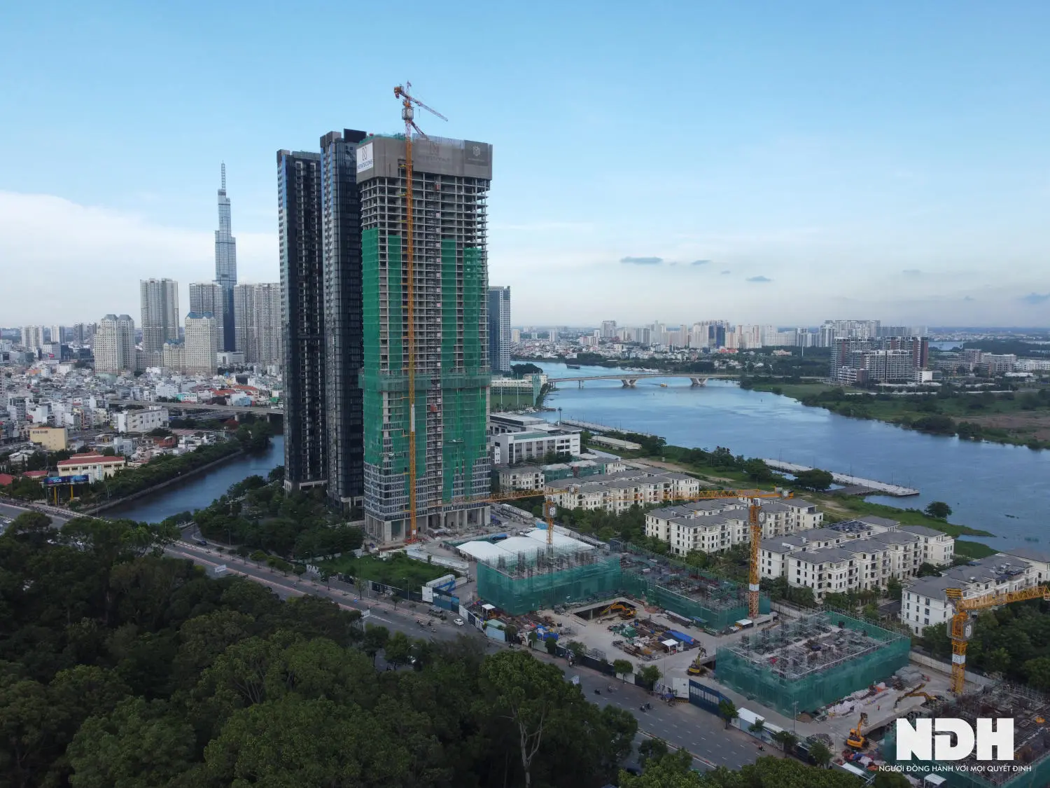 Ảnh từ trên cao: tháp căn hộ đang xây bên sông, nền là trung tâm thành phố
