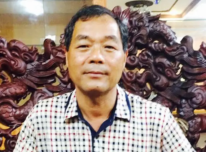 Chân dung người đàn ông mặc áo sơ mi kẻ, phía sau là bức tranh gỗ