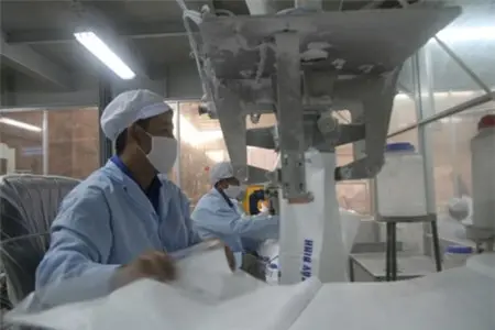 Công nhân đeo khẩu trang vận hành máy trong xưởng sản xuất sợi