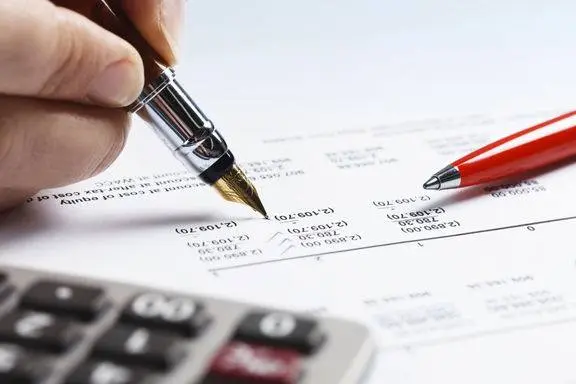 Hình minh họa bàn tay ký báo cáo tài chính bên máy tính cầm tay