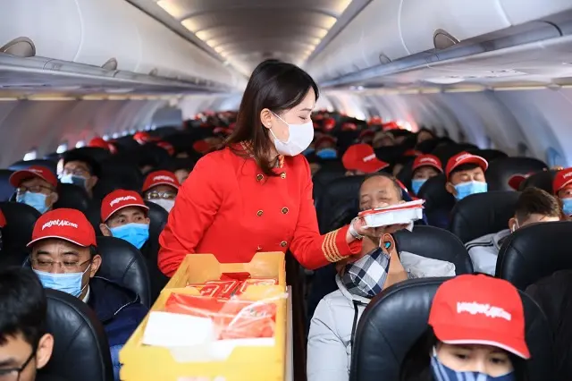 Tiếp viên phát quà cho hành khách đội mũ đỏ trên khoang máy bay