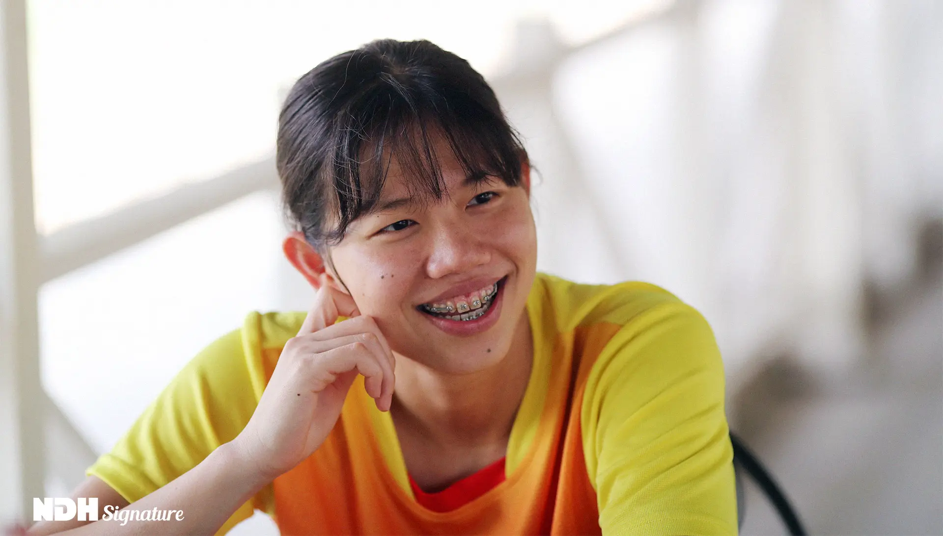 Ánh Viên chống cằm mỉm cười, mặc áo thể thao vàng cam