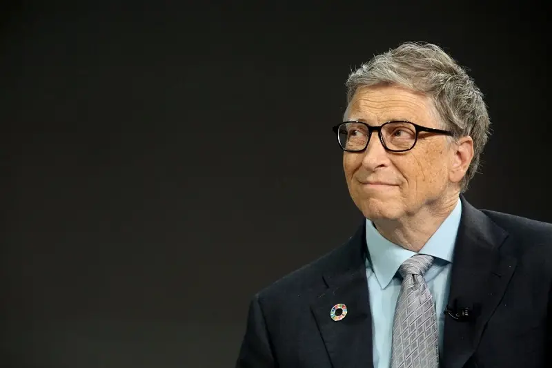 Bill Gates đeo kính, mặc vest và cà vạt xám trên nền tối