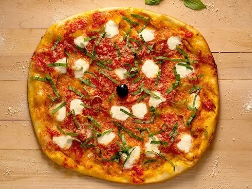 Chiếc pizza phô mai và lá húng trên mặt gỗ