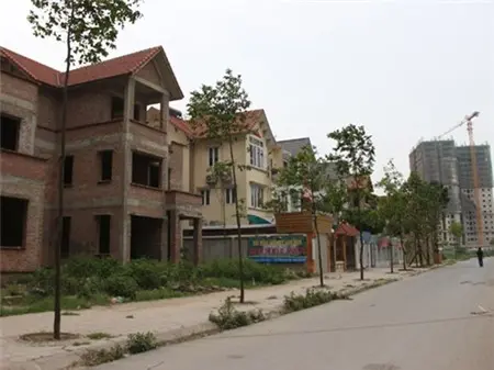 Dãy biệt thự xây dở bỏ trống bên đường, cao ốc đang thi công phía sau