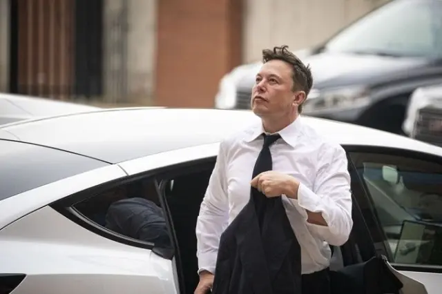 Elon Musk mặc sơ mi trắng bước ra từ xe Tesla màu trắng