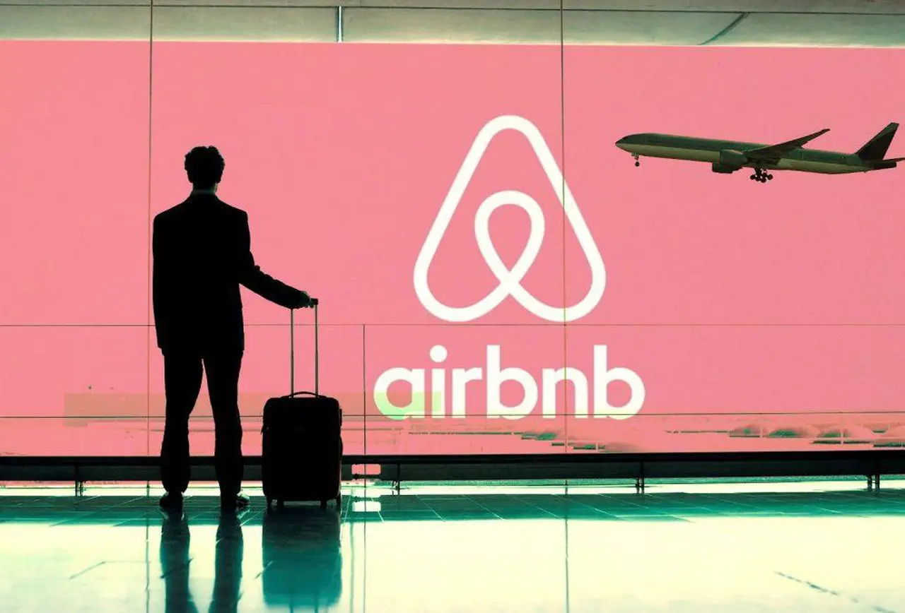 Hành khách kéo vali trước biển logo Airbnb ở sân bay