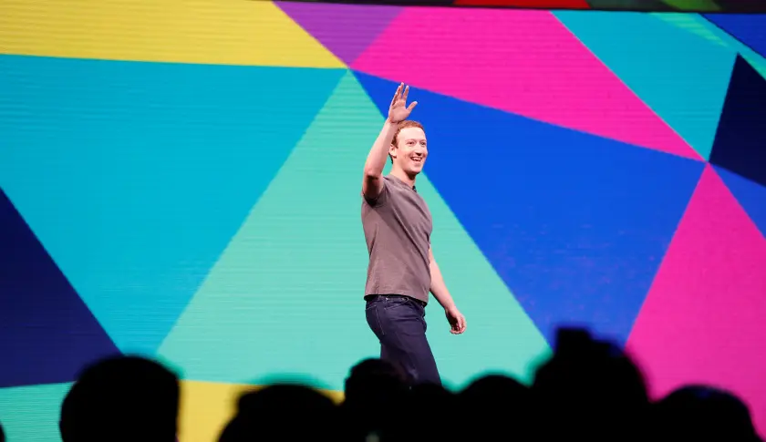 Mark Zuckerberg vẫy tay trên sân khấu có màn hình nhiều màu