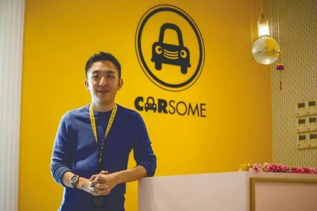 Người đàn ông đeo thẻ đứng trước logo Carsome trên tường vàng