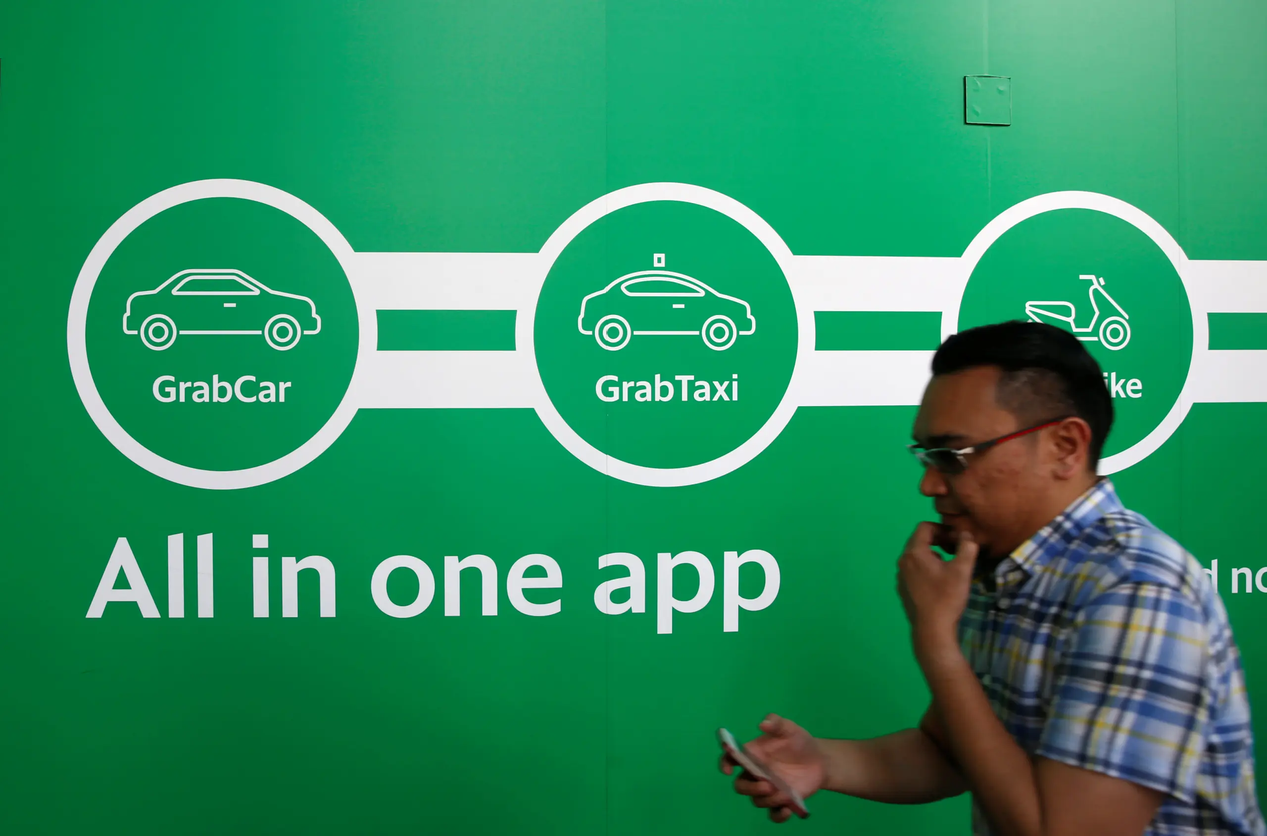 Người đàn ông đi ngang bức tường quảng cáo Grab màu xanh lá