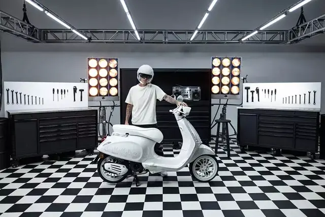 Người đội mũ bảo hiểm đứng cạnh xe Vespa trắng trong xưởng