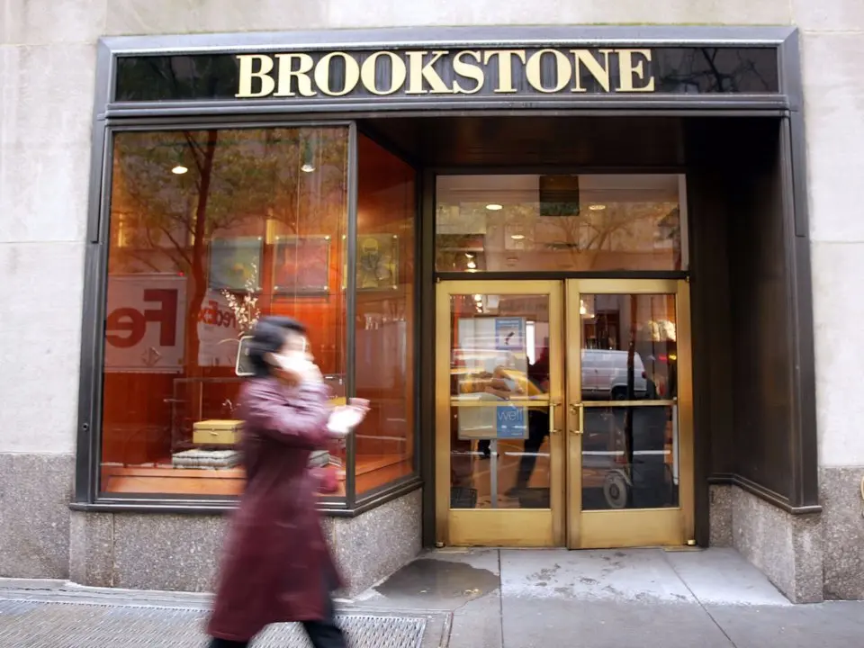 Người phụ nữ đi ngang cửa hàng Brookstone cửa kính khung vàng