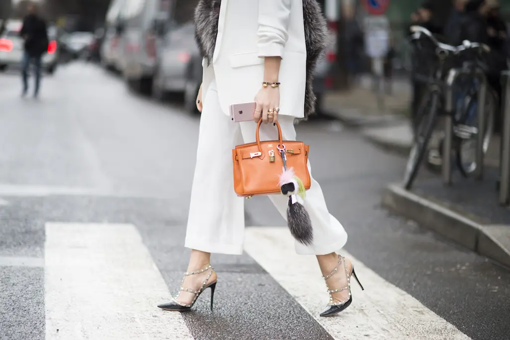 Người phụ nữ mặc đồ trắng xách túi Hermès màu cam qua đường