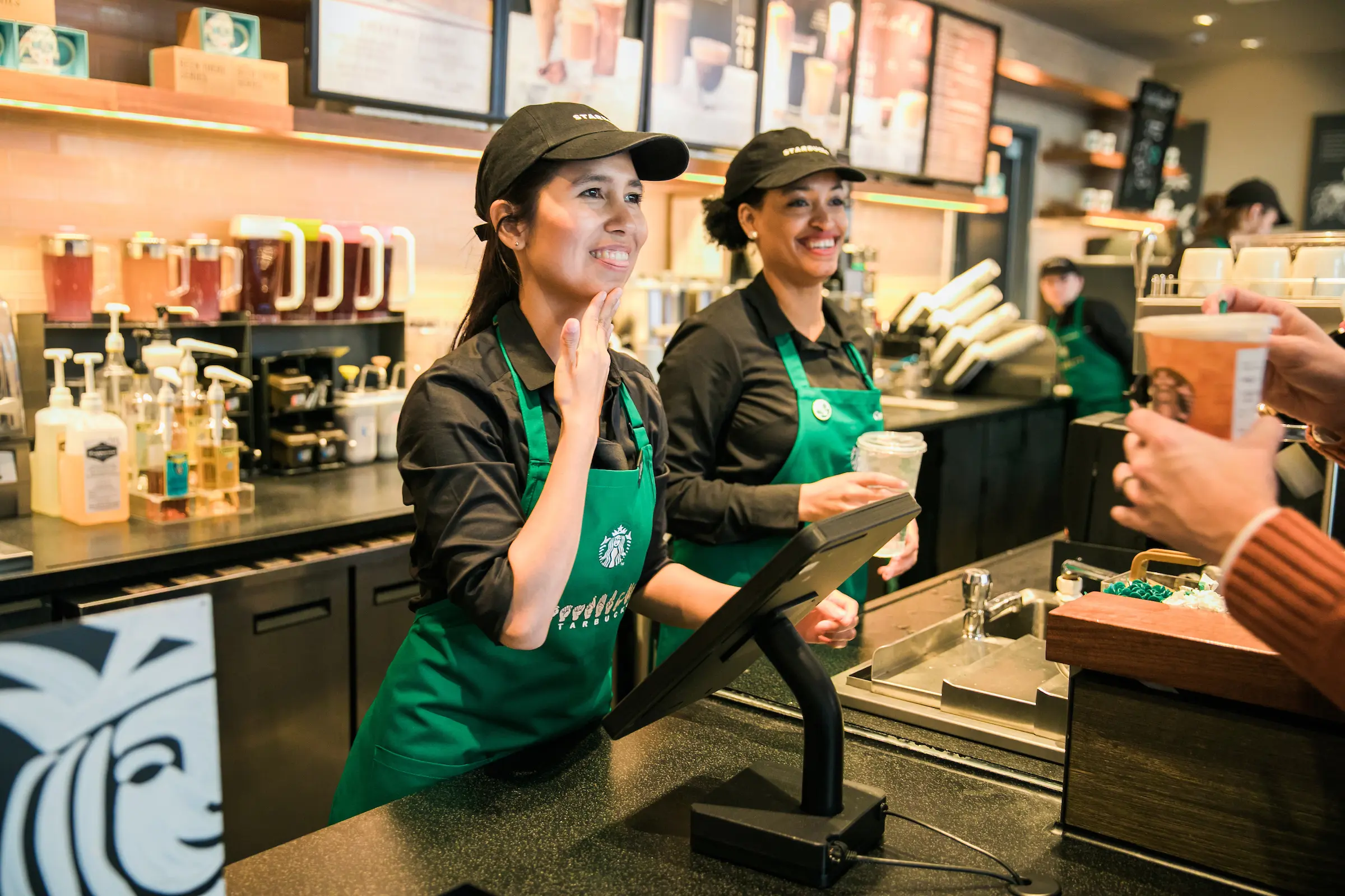 Nhân viên Starbucks mặc tạp dề xanh ra dấu tay tại quầy