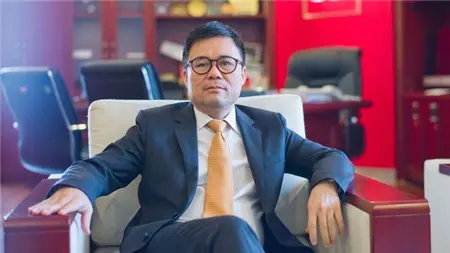 Ông Nguyễn Duy Hưng đeo kính, mặc vest, ngồi trên ghế bành
