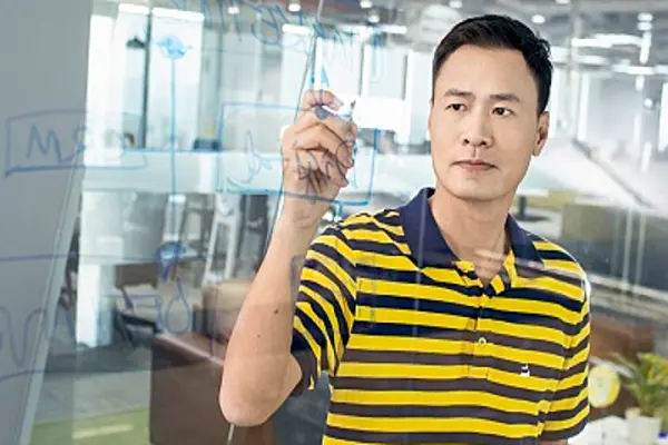 Ông Trần Thanh Hải mặc áo kẻ sọc vàng đen viết lên bảng kính