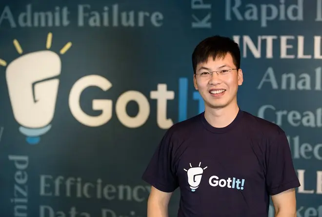 Trần Việt Hùng mặc áo thun đứng trước tường logo GotIt