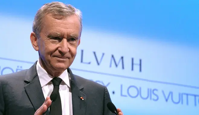 Tỷ phú Bernard Arnault đứng trước phông nền có logo LVMH