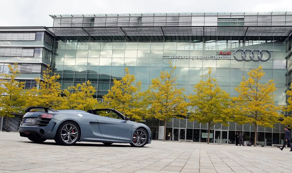 Xe Audi mui trần màu xám đậu trước tòa nhà kính có logo Audi