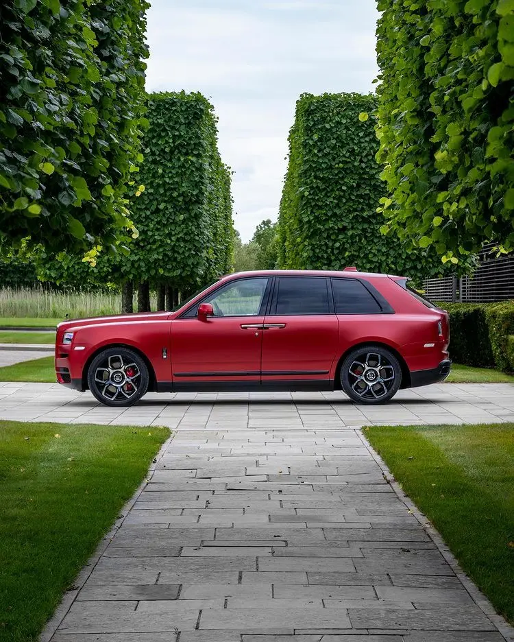 Xe Rolls-Royce Cullinan màu đỏ đỗ giữa hàng cây xanh